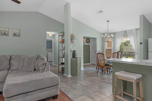 living room featuring ceiling fan with notable chandelier, lofted ceiling, light tile patterned floors, and washer / clothes dryer