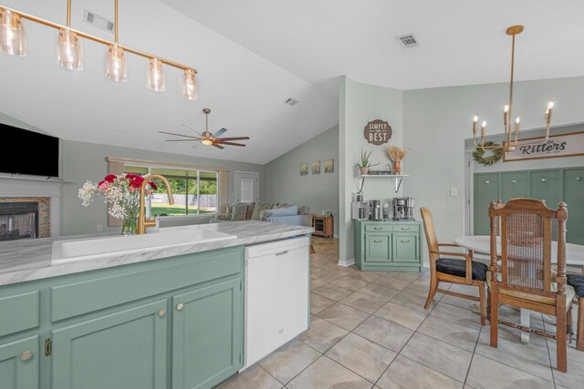 kitchen with ceiling fan with notable chandelier, white dishwasher, sink, a stone fireplace, and vaulted ceiling