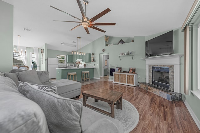 living room with lofted ceiling, ceiling fan with notable chandelier, dark hardwood / wood-style floors, and a stone fireplace