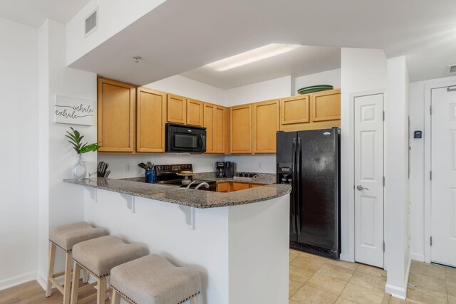 kitchen with dark stone countertops, light tile patterned floors, black appliances, kitchen peninsula, and a breakfast bar