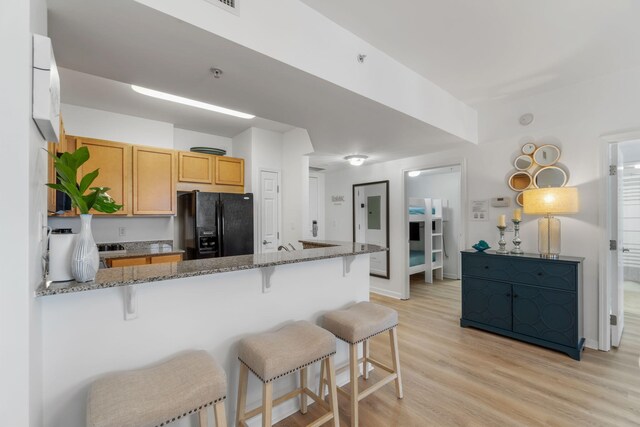 kitchen with light wood-type flooring, a kitchen bar, kitchen peninsula, stone countertops, and black fridge