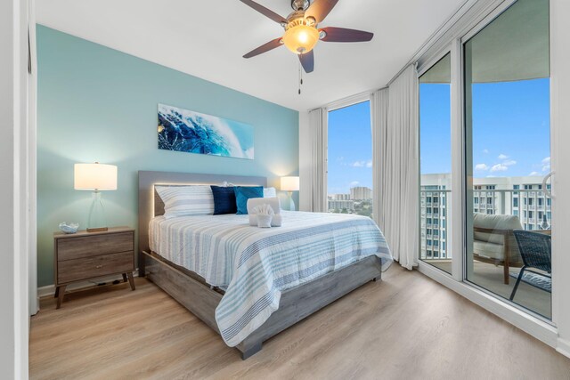 bedroom with light wood-type flooring, access to exterior, ceiling fan, and a wall of windows