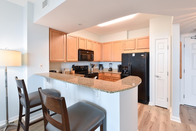 kitchen featuring black appliances, kitchen peninsula, light hardwood / wood-style flooring, and light stone countertops