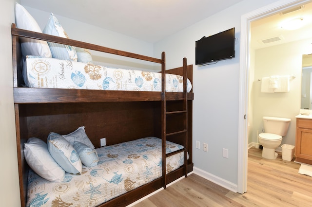 bedroom featuring light wood-type flooring, baseboards, visible vents, and connected bathroom