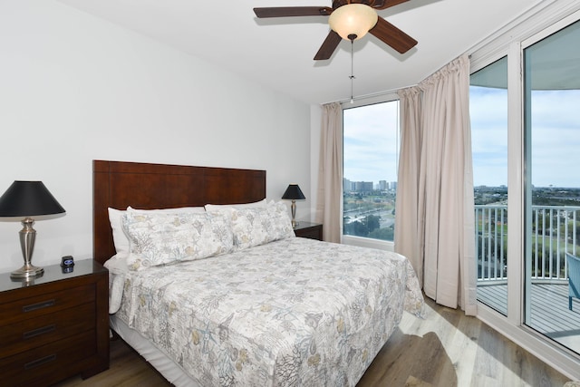 bedroom with access to exterior, a view of city, wood finished floors, and ceiling fan