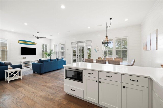 kitchen featuring built in microwave, ceiling fan with notable chandelier, wood-type flooring, hanging light fixtures, and white cabinets