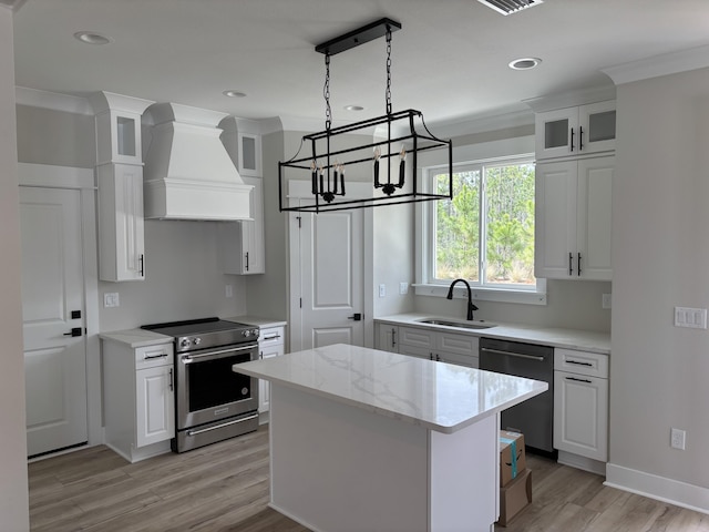 kitchen with a sink, custom range hood, appliances with stainless steel finishes, white cabinetry, and a notable chandelier