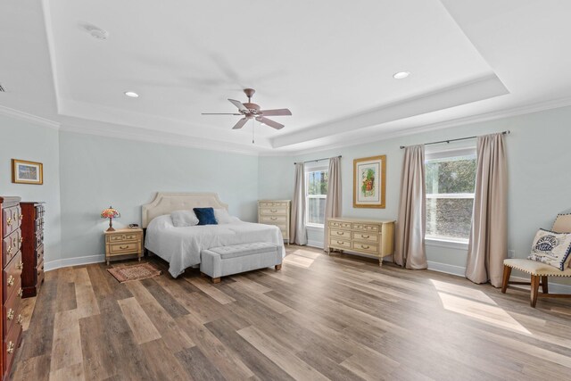 bedroom with ornamental molding, wood-type flooring, and a raised ceiling