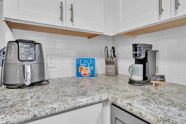 room details featuring tasteful backsplash, light stone counters, and white cabinets