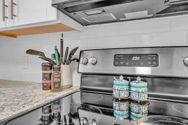 interior details featuring electric range, tasteful backsplash, light stone countertops, and white cabinets