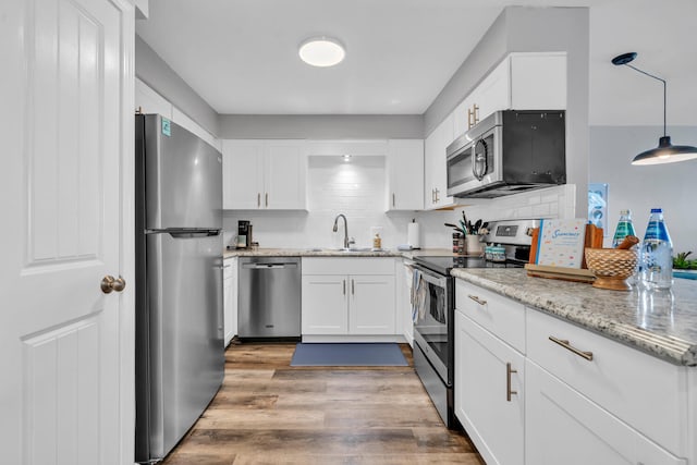 kitchen with decorative backsplash, appliances with stainless steel finishes, wood finished floors, white cabinetry, and a sink