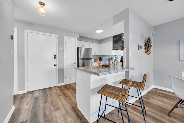 kitchen with a breakfast bar area, dark wood-type flooring, freestanding refrigerator, white cabinetry, and a peninsula