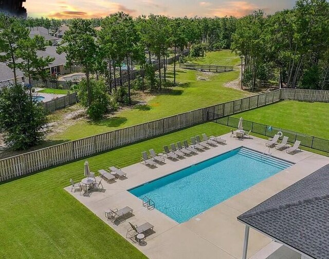 pool at dusk featuring a lawn and a patio area