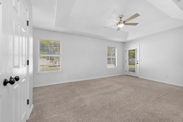 carpeted empty room with a wealth of natural light, ceiling fan, and a tray ceiling