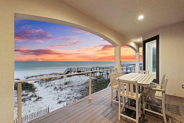 view of dock featuring a water view, a balcony, and a view of the beach