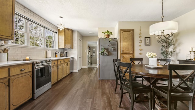 kitchen with dark wood finished floors, light countertops, backsplash, appliances with stainless steel finishes, and brown cabinetry