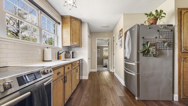 kitchen featuring dark wood-style flooring, brown cabinets, stainless steel appliances, decorative backsplash, and a sink