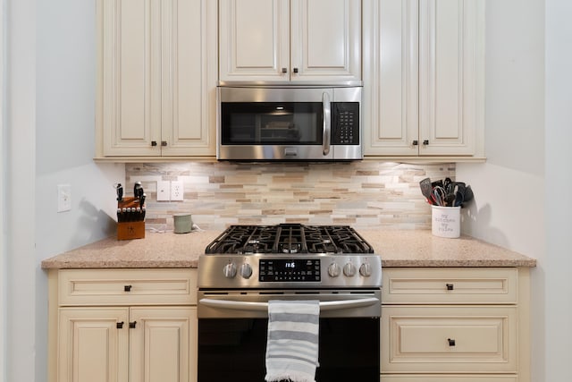 kitchen with light stone counters, stainless steel appliances, cream cabinets, and tasteful backsplash