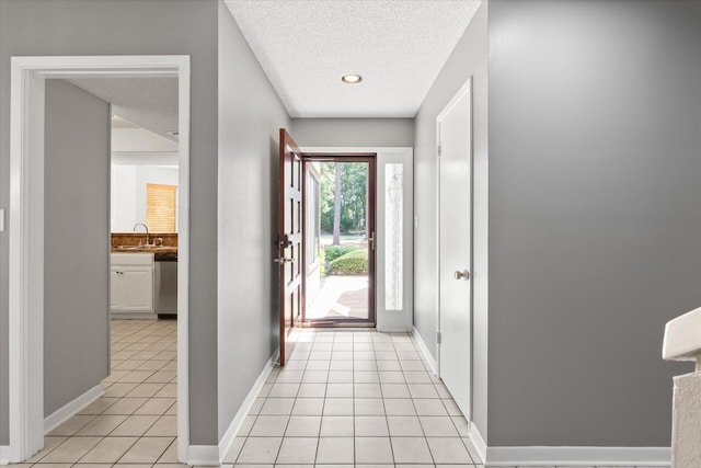 doorway to outside with a textured ceiling, sink, and light tile patterned floors