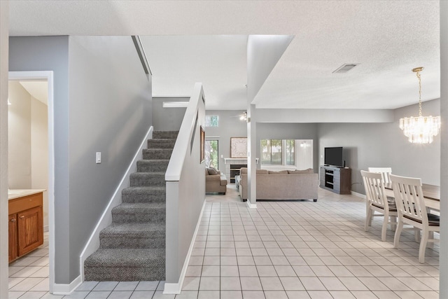 stairway with tile patterned flooring, a fireplace, an inviting chandelier, and a textured ceiling