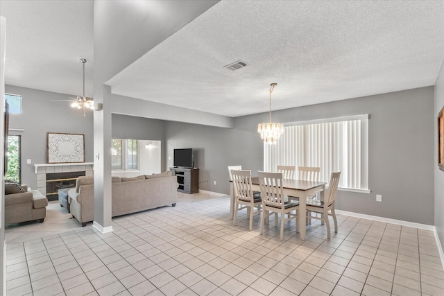 dining room with a textured ceiling, ceiling fan with notable chandelier, a tile fireplace, and light tile patterned floors