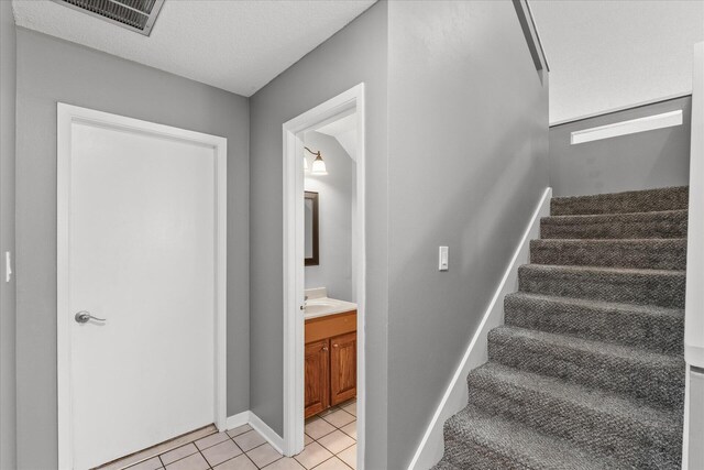 staircase featuring a textured ceiling, sink, and tile patterned floors