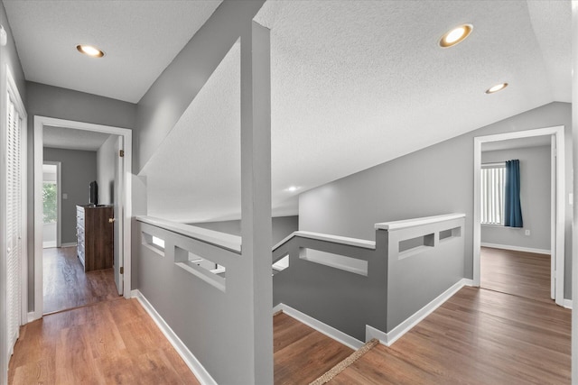 hall with lofted ceiling, hardwood / wood-style floors, and a textured ceiling