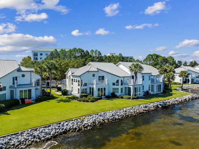 back of property with a balcony, a water view, and a yard