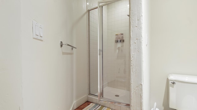 full bath with toilet, a stall shower, and baseboards