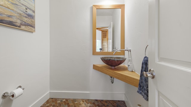 bathroom featuring brick floor, a sink, and baseboards