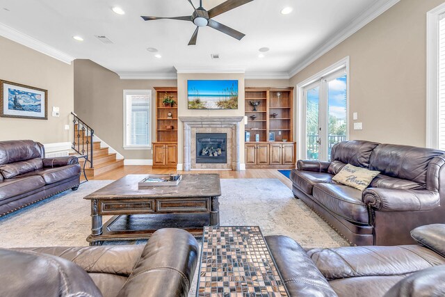 living room featuring light wood-type flooring, built in shelves, ceiling fan, and crown molding