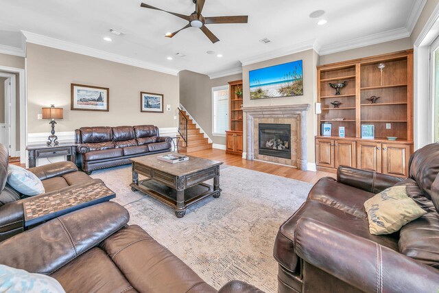 living room featuring a fireplace, built in shelves, ornamental molding, ceiling fan, and light wood-type flooring