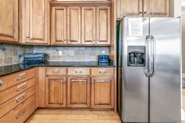 kitchen with light wood-type flooring, stainless steel fridge, backsplash, and dark stone counters