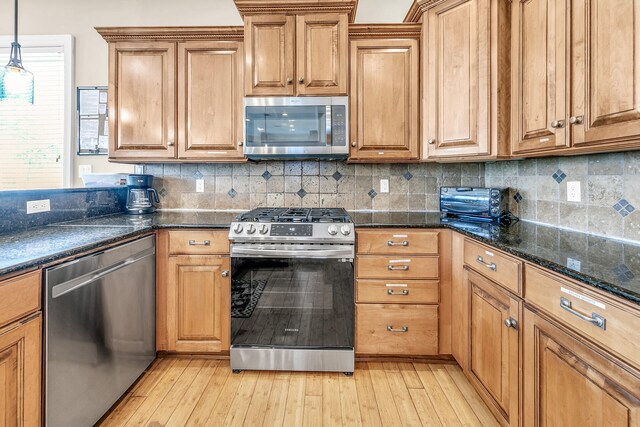 kitchen with appliances with stainless steel finishes, light hardwood / wood-style flooring, backsplash, and decorative light fixtures