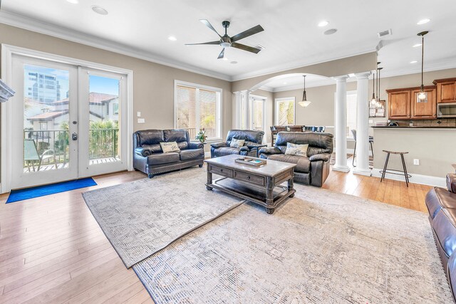 living room featuring crown molding, ceiling fan, light wood-type flooring, and ornate columns