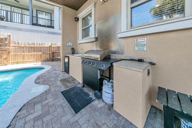 view of patio / terrace with a fenced in pool, sink, a grill, and a balcony