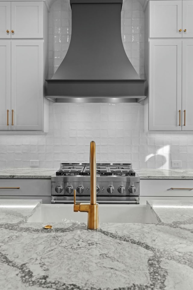 kitchen with white cabinets, decorative backsplash, premium range hood, and light stone counters