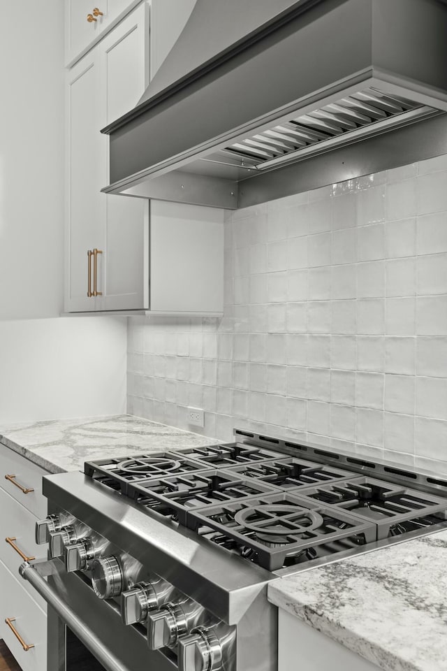 kitchen with light stone countertops, tasteful backsplash, custom range hood, high end stainless steel range oven, and white cabinetry