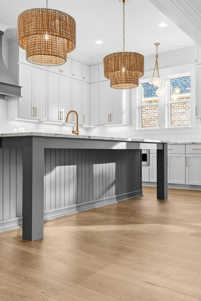 kitchen with light wood-type flooring, tasteful backsplash, light stone counters, and hanging light fixtures