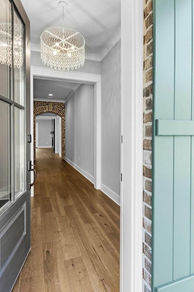 hall with hardwood / wood-style floors, crown molding, brick wall, and a chandelier