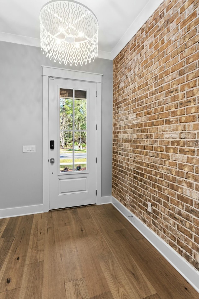 doorway to outside with hardwood / wood-style floors, ornamental molding, brick wall, and an inviting chandelier