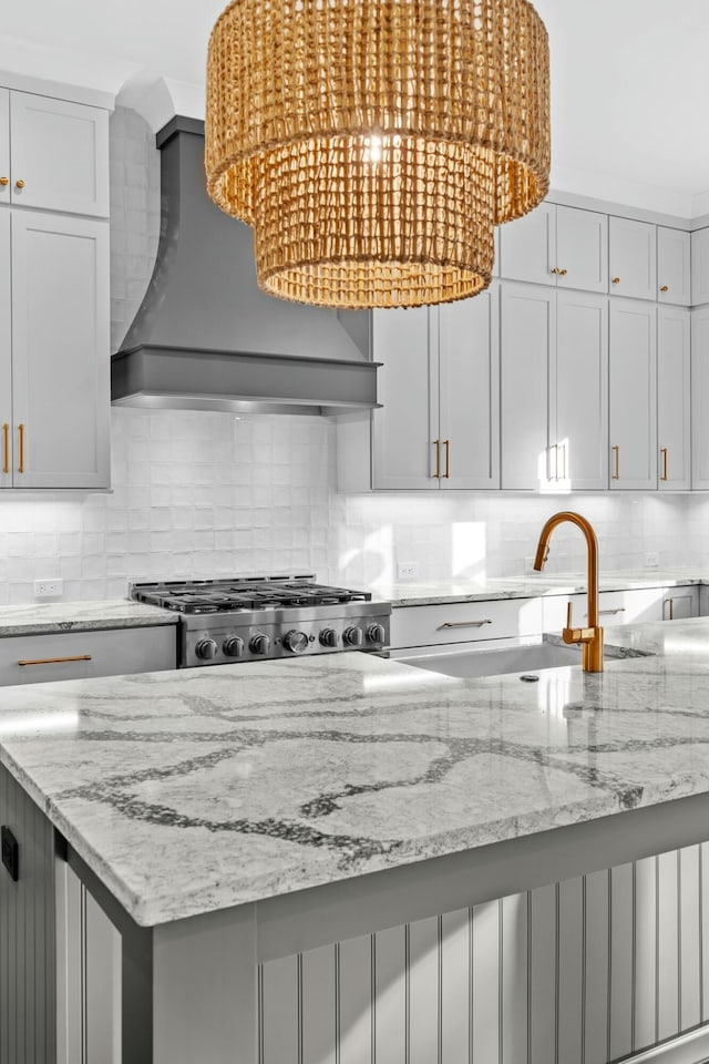 kitchen with stove, sink, decorative backsplash, light stone countertops, and custom range hood