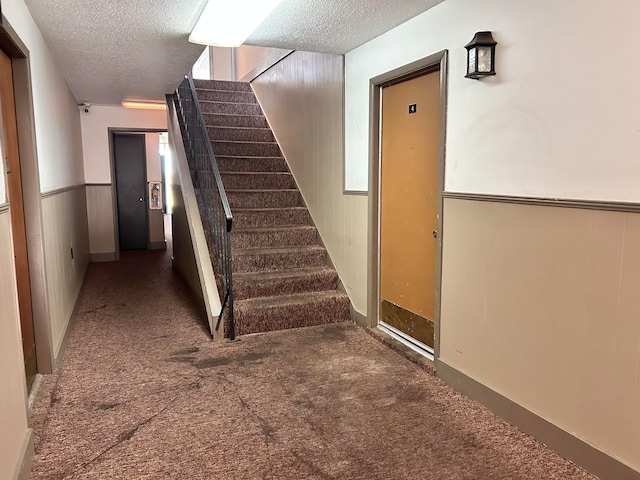 stairs featuring carpet, wooden walls, and a textured ceiling