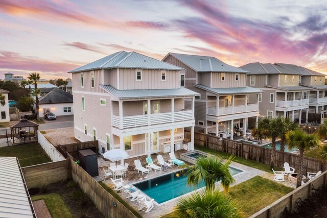 back house at dusk featuring a fenced in pool, a patio area, and a balcony