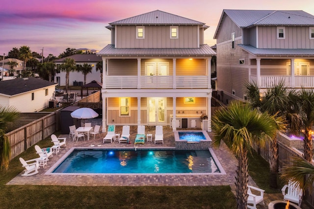 back house at dusk with a balcony, a patio area, and a swimming pool with hot tub