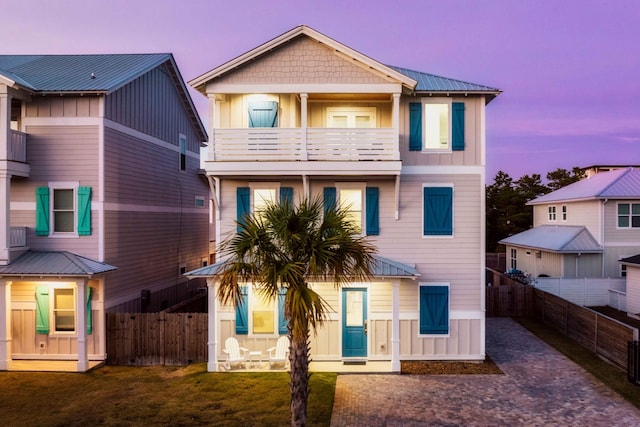 back of property at dusk with a balcony, driveway, fence, and board and batten siding