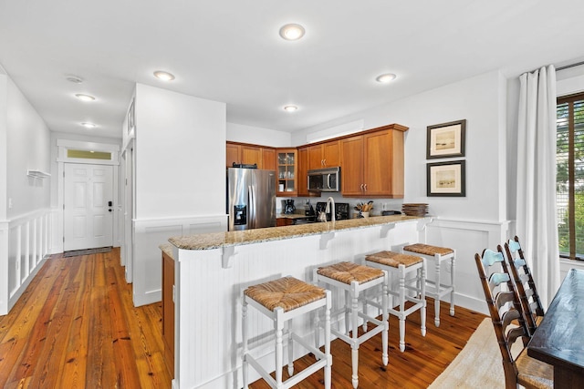 kitchen with hardwood / wood-style floors, light stone countertops, stainless steel appliances, kitchen peninsula, and a breakfast bar