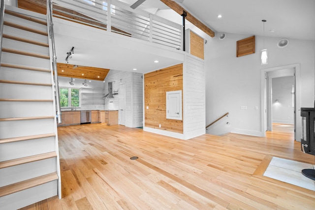 unfurnished living room featuring wood walls, high vaulted ceiling, beam ceiling, and light hardwood / wood-style floors