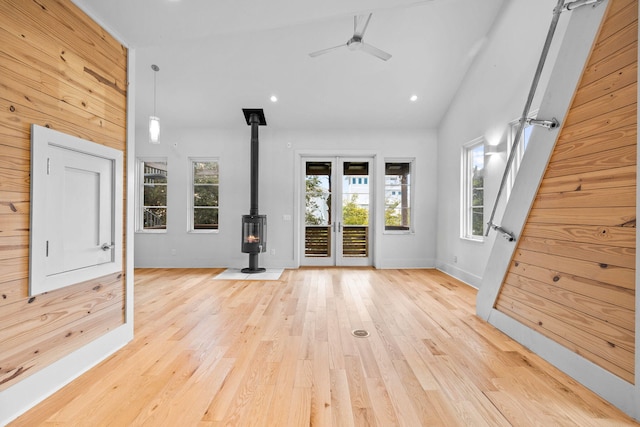 unfurnished living room with high vaulted ceiling, a wood stove, ceiling fan, french doors, and light hardwood / wood-style floors