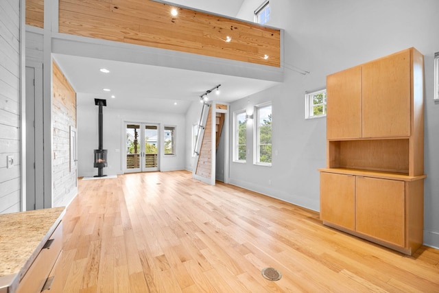 unfurnished living room with light wood-type flooring, high vaulted ceiling, and a wood stove